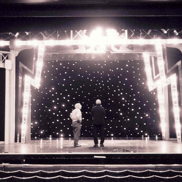 Two people stood on the stage looking toward the back of the stage area which is lit up to look like stars